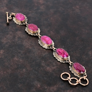 May include: A silver bracelet with five oval-shaped pink gemstones set in ornate silver frames. The bracelet has a clasp closure.