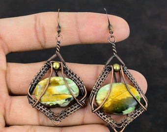 May include: A pair of copper wire wrapped earrings with green and yellow gemstone accents. The earrings are teardrop shaped and have a woven wire design.