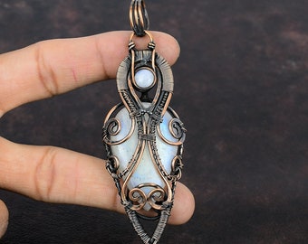 May include: A white moonstone pendant with a copper wire wrap design. The pendant is in the shape of a teardrop and has a delicate, intricate design.