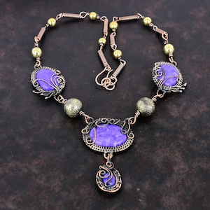 May include: A handcrafted necklace featuring purple oval and round stones, accented with copper wire and brass beads. The necklace has a unique, artistic design with intricate wirework and a vintage aesthetic.
