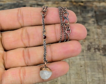 May include: A copper chain necklace with a white gemstone pendant and a red gemstone accent. The necklace has a lobster clasp closure.