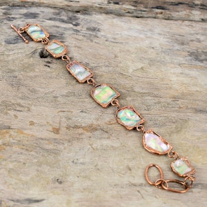 May include: A copper bracelet with iridescent abalone shell accents. The bracelet has a clasp closure and is made of copper wire.