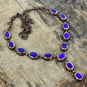 May include: A copper-toned necklace featuring oval-shaped, deep blue gemstones. The stones are set in copper-colored bezels and linked by a delicate chain. The necklace has a Y-shaped pendant design, perfect for adding a touch of elegance.