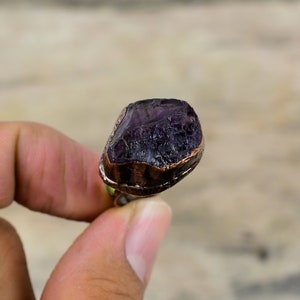 May include: A ring with a large, raw amethyst stone set in a copper band. The stone is a deep purple color and has a rough, natural texture.