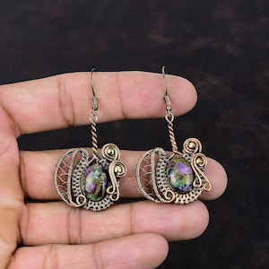 May include: A pair of copper wire wrapped earrings with a green, pink, and purple gemstone in the center of each earring.