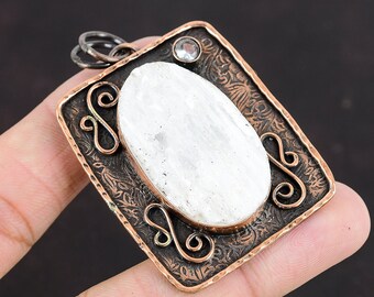 May include: A white oval gemstone pendant with a copper frame. The frame has a textured design with swirls and a small clear rhinestone.