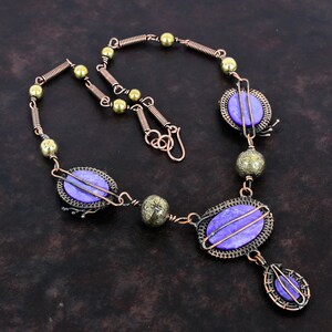 May include: A handcrafted necklace featuring oval, lavender-colored stones set in copper wire frames. The necklace includes copper wire, brass beads, and a teardrop pendant. The design has a vintage, artisan aesthetic.
