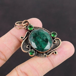 May include: A copper pendant with a large green gemstone surrounded by smaller green gemstones. The pendant has an intricate design with swirls and floral motifs.