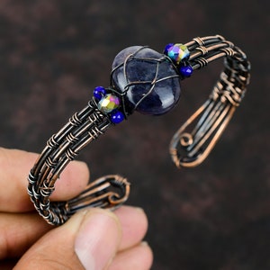 May include: A copper wire wrapped bracelet with a dark purple gemstone and iridescent blue glass beads.