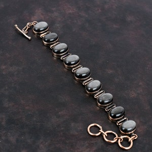 Könnte beinhalten: Ein Armband aus schwarzen Edelsteinen mit einem silbernen Verschluss. Das Armband besteht aus ovalen Steinen, die in Silber gefasst sind.
