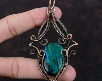 May include: A copper wire wrapped pendant featuring a green and blue gemstone. The pendant is in the shape of a diamond with intricate wirework.