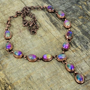 May include: A copper necklace with a pendant and oval-shaped iridescent stones. The stones have a rainbow of colours, including purple, blue, green, and pink.