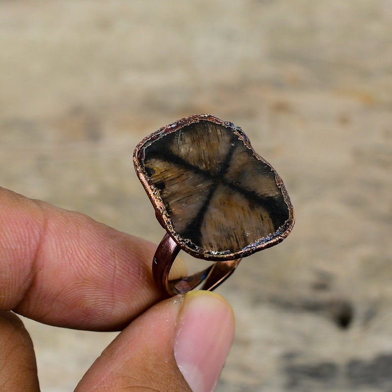 Pu&ograve; includere: Un anello in rame con una pietra preziosa marrone e nera a forma di stella incastonata al centro. L'anello &egrave; in rame e ha una finitura rustica.