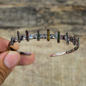 May include: A copper bracelet with a row of green, black, and gold tourmaline gemstones set in the metal.