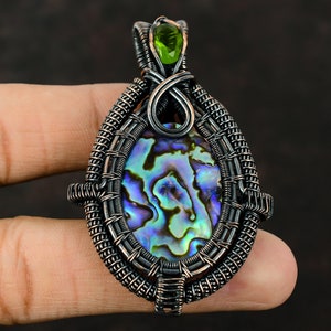 May include: A silver wire wrapped pendant featuring a iridescent abalone shell with a green gemstone accent.