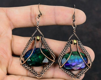 Puede incluir: Un par de pendientes de alambre de cobre con una piedra preciosa verde y azul iridiscente en cada uno. Los pendientes tienen forma de diamante con un diseño de alambre tejido.