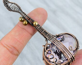 May include: A copper wire wrapped pendant featuring a purple amethyst gemstone in the shape of a heart. The pendant is shaped like a guitar with copper wire details and two small gold beads.