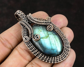 May include: A copper wire wrapped pendant featuring a blue-green labradorite gemstone. The wire is woven into a detailed pattern with swirls and a basket weave design.