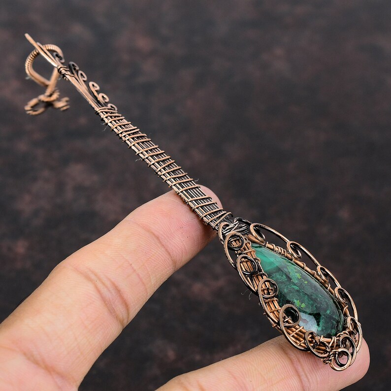 May include: A handcrafted copper pendant with a teardrop-shaped green stone. The pendant features intricate wire wrapping and a decorative bail. The stone is approximately 3.8 cm long, and the overall design is ornate and detailed.