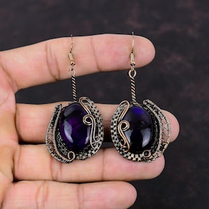May include: A pair of purple gemstone earrings with copper wire wrapping. The earrings are oval shaped and have a delicate, intricate design.