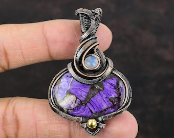 May include: A handcrafted pendant featuring a large, oval-shaped purple stone with gold flecks, encased in intricate copper wire. A small, round, light blue stone is set above the purple stone, with a gold bead at the bottom.
