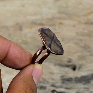 Pu&ograve; includere: Un anello in rame con una pietra preziosa a forma di stella marrone e nera incastonata al centro.