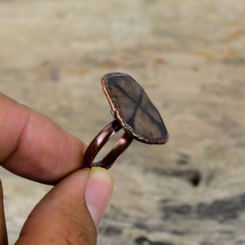 Pu&ograve; includere: Un anello in rame con una pietra preziosa a forma di stella marrone e nera incastonata al centro.