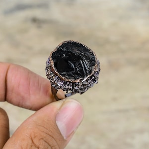 May include: A black gemstone ring with a copper setting and a border of small purple beads.