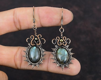 May include: A pair of handcrafted earrings featuring oval-shaped labradorite stones. The stones are set in a copper-colored wire frame with a sunburst design. The earrings have a decorative swirl and bead detail at the top and are suspended from a simple hook.