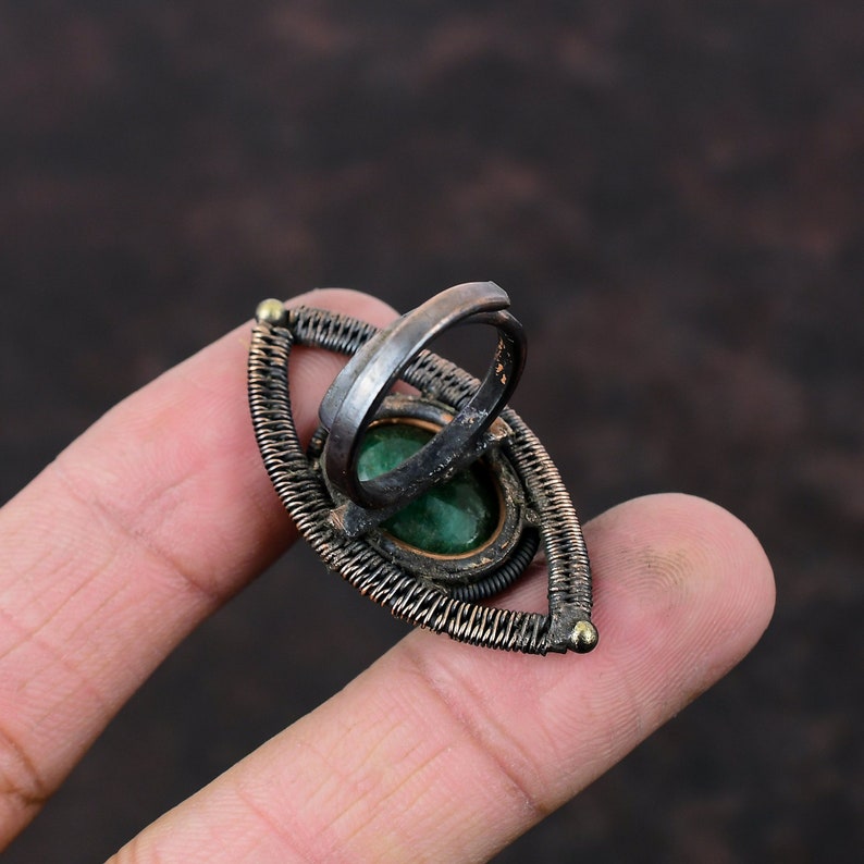 May include: A silver ring with a green gemstone set in a wire-wrapped design. The ring is shaped like an eye and has a gold accent.