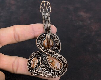 May include: A copper wire wrapped guitar pendant with brown and white agate stones. The pendant is intricately detailed and has a unique design.