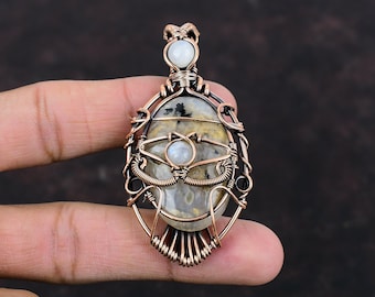 May include: A copper wire wrapped pendant featuring a white and gray agate stone with a smaller white moonstone accent. The pendant has a delicate, intricate design.