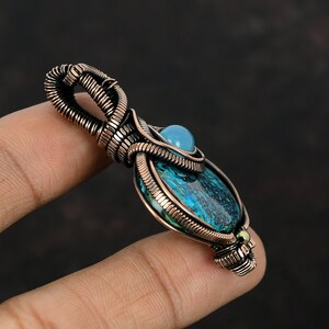 May include: A copper wire wrapped pendant featuring a blue and green gemstone with a smaller blue gemstone at the top.