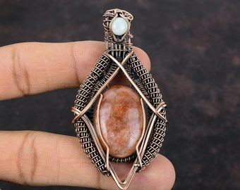May include: A copper wire wrapped pendant featuring a sunstone cabochon and a white opal accent. The pendant is in the shape of a diamond.