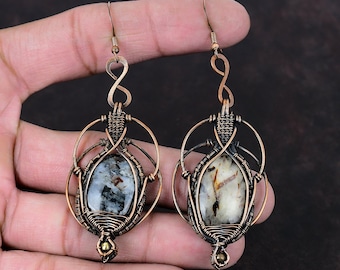 May include: A pair of copper wire wrapped earrings with a white and brown stone in each. The earrings are in the shape of an infinity symbol.