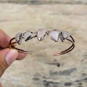 May include: A copper wire bracelet with five raw rose quartz stones set in the wire. The bracelet is open and adjustable.