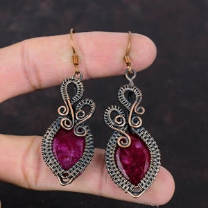 May include: A pair of dangle earrings with a pink and white stone set in a copper wire frame. The earrings have a delicate, intricate design.