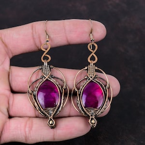 May include: A pair of copper wire wrapped earrings with a pink gemstone in the centre of each earring. The earrings are dangling and have a wire loop at the top.
