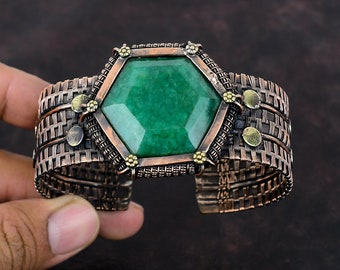 May include: A copper wire cuff bracelet with a large green gemstone in the center. The gemstone is set in a hexagonal frame with small gold accents.
