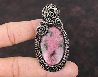 May include: A pink and black gemstone pendant wrapped in copper wire. The pendant is oval shaped and has a wire design around the edge.