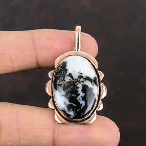 Peut inclure: Un pendentif en argent avec une pierre ovale noire et blanche sertie dans un cadre décoratif. La pierre présente un motif tourbillonnant de noir et de blanc.