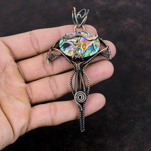 Op de afbeelding: Een hanger van koperdraad met een iriserende abalone-schelp. De hanger is gevormd als een gestileerde boom met een lange, dunne steel.
