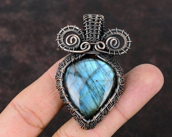 May include: A teardrop-shaped labradorite gemstone pendant wrapped in copper wire. The wire is twisted into intricate designs, creating a unique and eye-catching piece of jewelry.