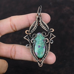 May include: A green and pink gemstone pendant with a copper wire design. The pendant is shaped like a teardrop and has a delicate, intricate design.