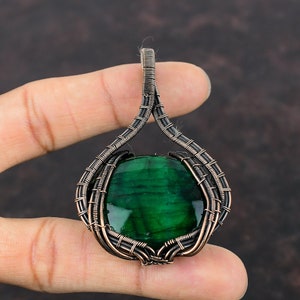 Puede incluir: Un colgante de piedra preciosa verde con un envoltorio de alambre de cobre y plata. El colgante tiene forma de lágrima y tiene un acabado liso y pulido.