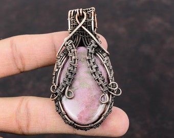 May include: A pink and green gemstone pendant wrapped in copper wire. The wire is woven into a delicate pattern around the stone, creating a unique and intricate design.