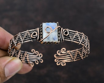 May include: A copper wire wrapped bracelet with a woven design and a rectangular moonstone gemstone in the center.