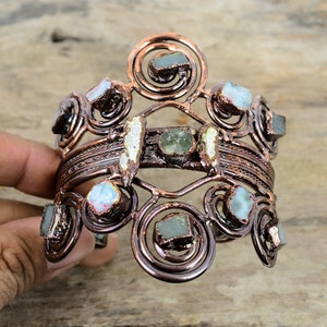 Può includere: Un braccialetto in filo di rame con un design decorativo che presenta più pietre preziose verdi e bianche.