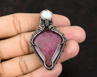 May include: A teardrop-shaped pink gemstone pendant wrapped in copper wire with a smaller white gemstone at the top.
