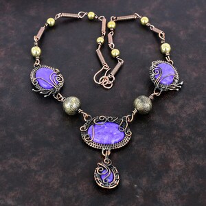 May include: A handcrafted necklace featuring purple oval and round stones, accented with copper wire and brass beads. The necklace has a unique, artistic design with intricate wirework and a pendant drop.